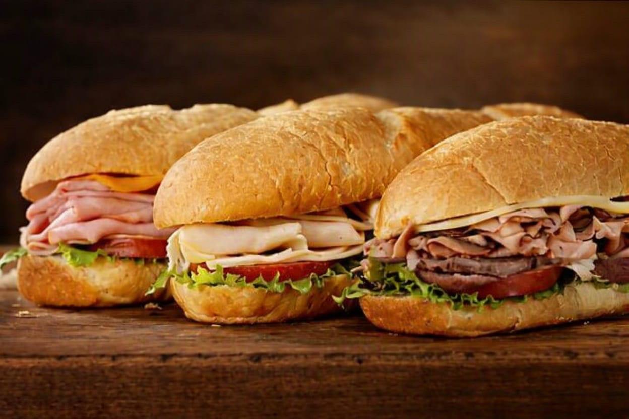 Three deli subs stacked with meat, cheese, lettuce and tomato